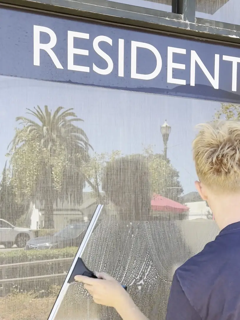 High Tide crew member squeegeeing a downtown storefront window under the shop's sign