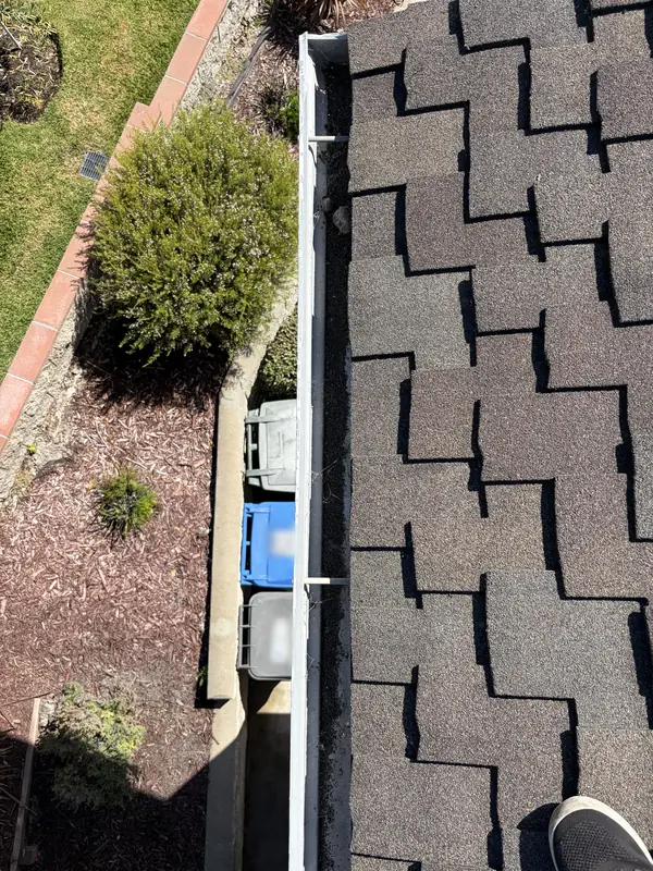Before: A home's gutter packed with leaves and roof grit along a shingle roof, before a High Tide cleaning