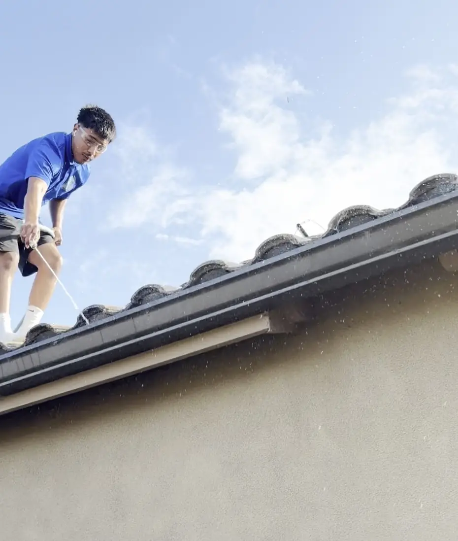 High Tide crew member on a tile roof edge, clearing the gutter above a backyard fence