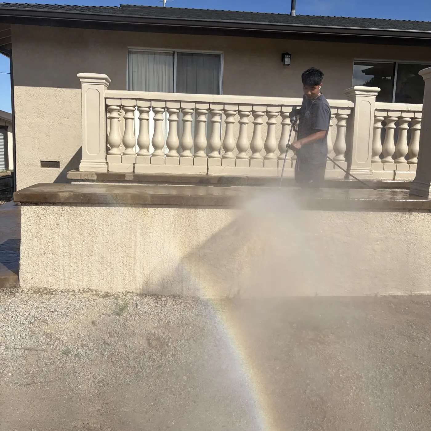 Crew member rinsing a home's stucco wall and patio with a low-pressure spray