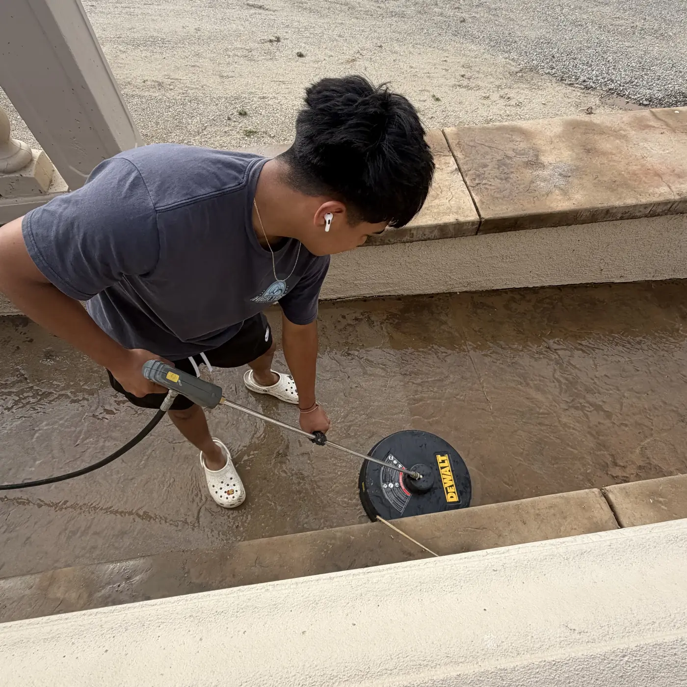 Crew member pressure-washing concrete steps with a surface cleaner
