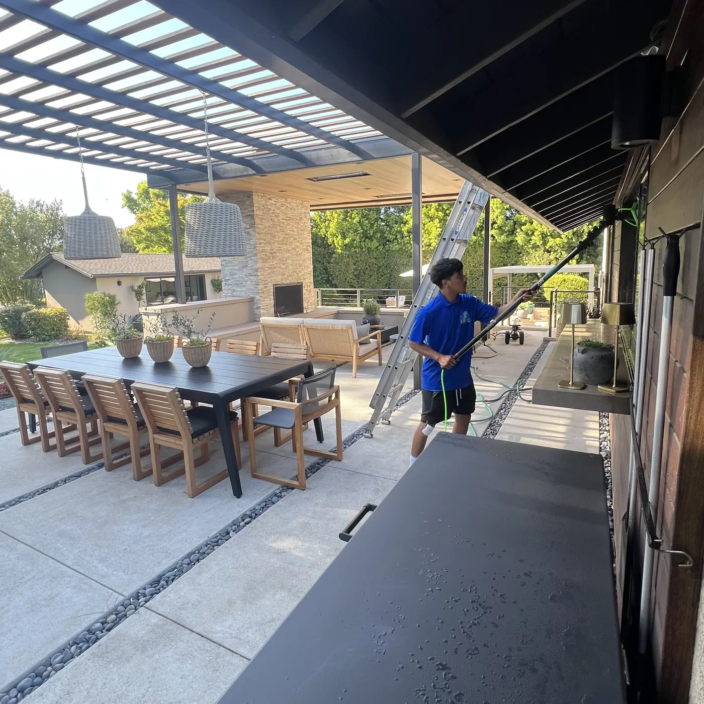 Crew member cleaning a home's back-patio windows with a pole, ladder set up nearby