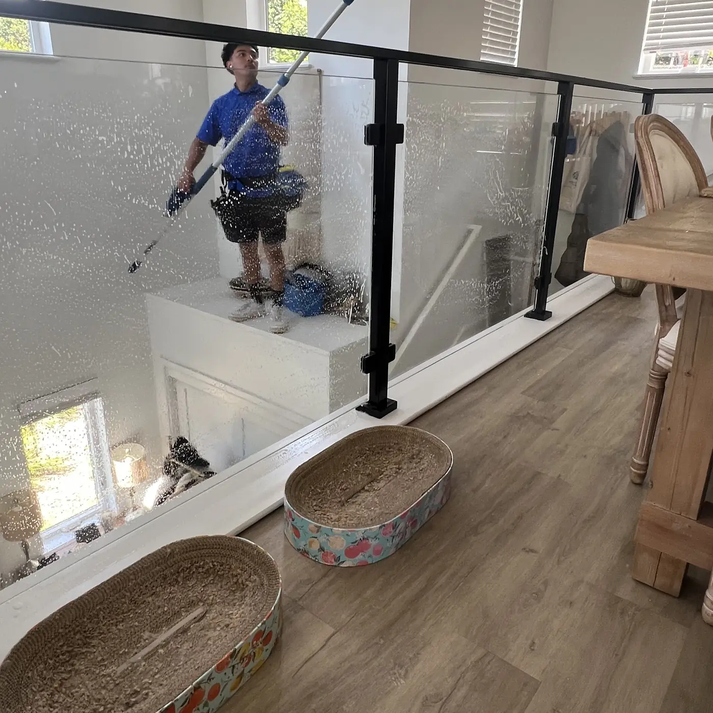 Crew member cleaning an indoor glass stair railing with a squeegee pole