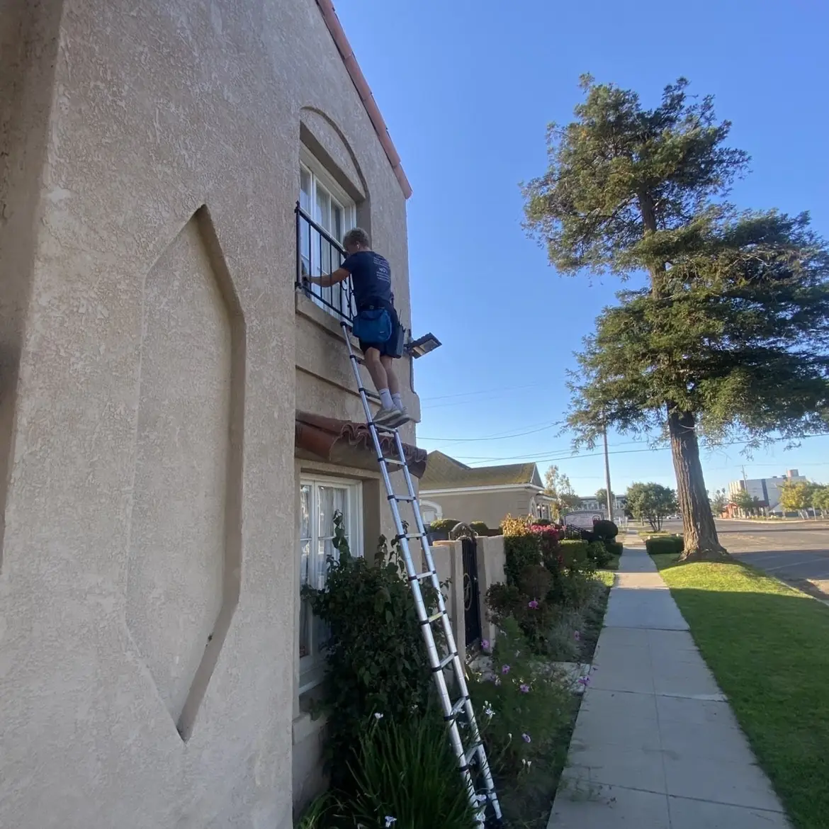 Crew member on a ladder cleaning a second-story window on a stucco home