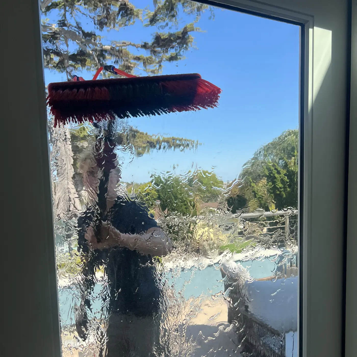 High Tide crew member scrubbing a glass patio door with a soapy brush, seen from inside the home, window cleaning in Pismo Beach, CA