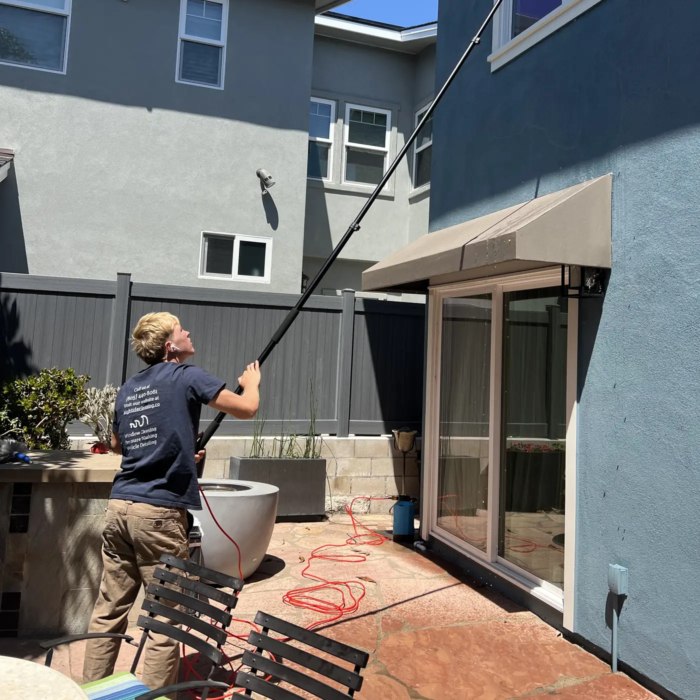 High Tide crew member cleaning a second-story window from the patio with a water-fed pole